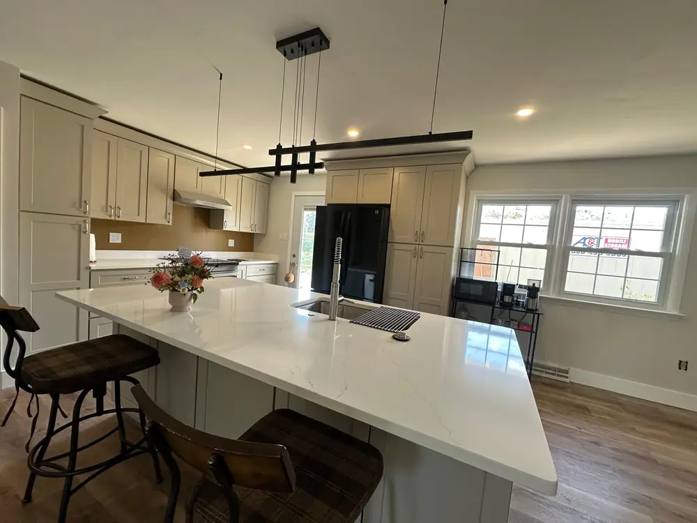 Large white quartz island with bar stools under a linear pendant
